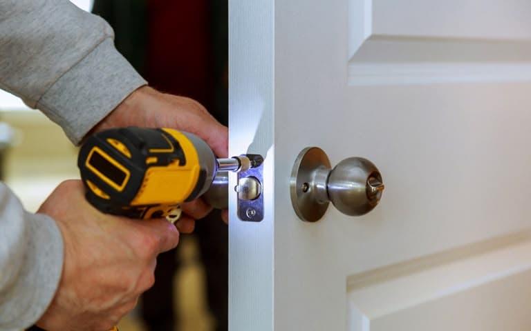 Cordless drill fitting a new latch into the edge of a door during a lock installation